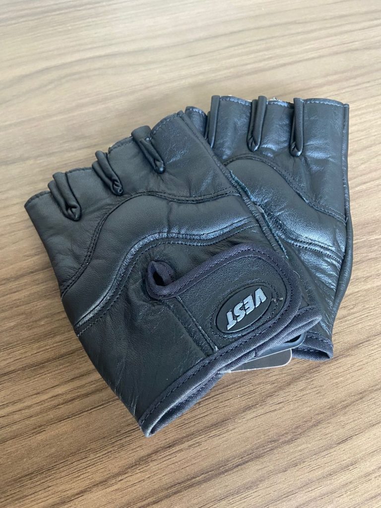 Um par de luvas de couro pretas sem dedos da marca VEST em uma mesa de madeira.