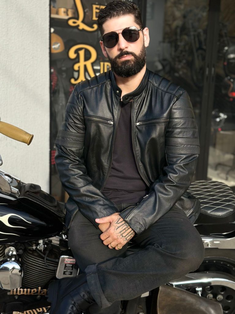 Homem barbudo estiloso sentado em uma motocicleta com jaqueta de couro e óculos de sol