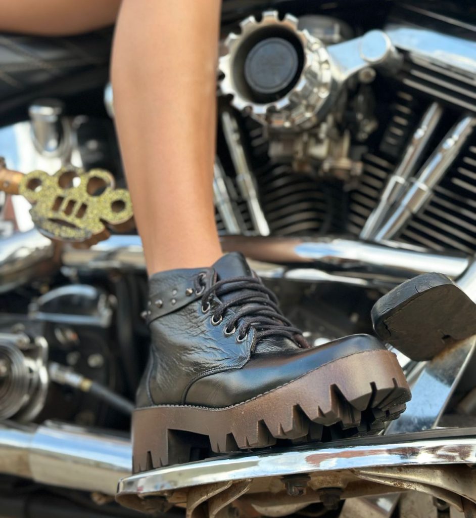 Bota de couro preta com sola tratorada marrom em cima de uma moto.