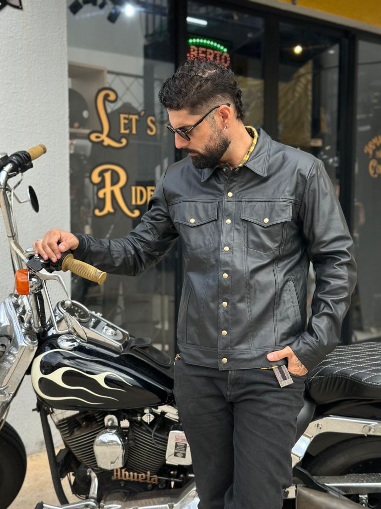 Homem estiloso em jaqueta de couro preta e jeans pretos ao lado de uma motocicleta